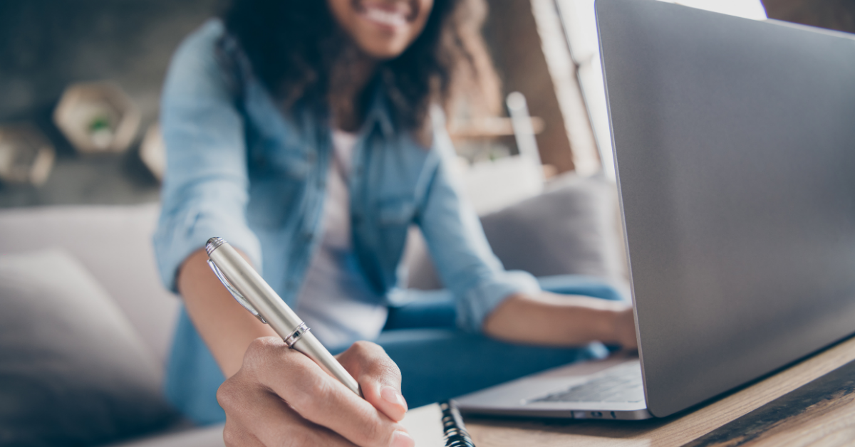 woman at computer writing out notes on a notepad